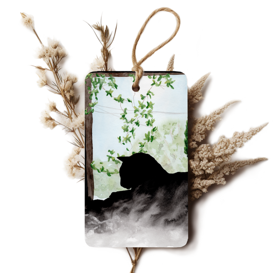 Decorative tag with a black cat silhouette and greenery, surrounded by dried plants on a white background.