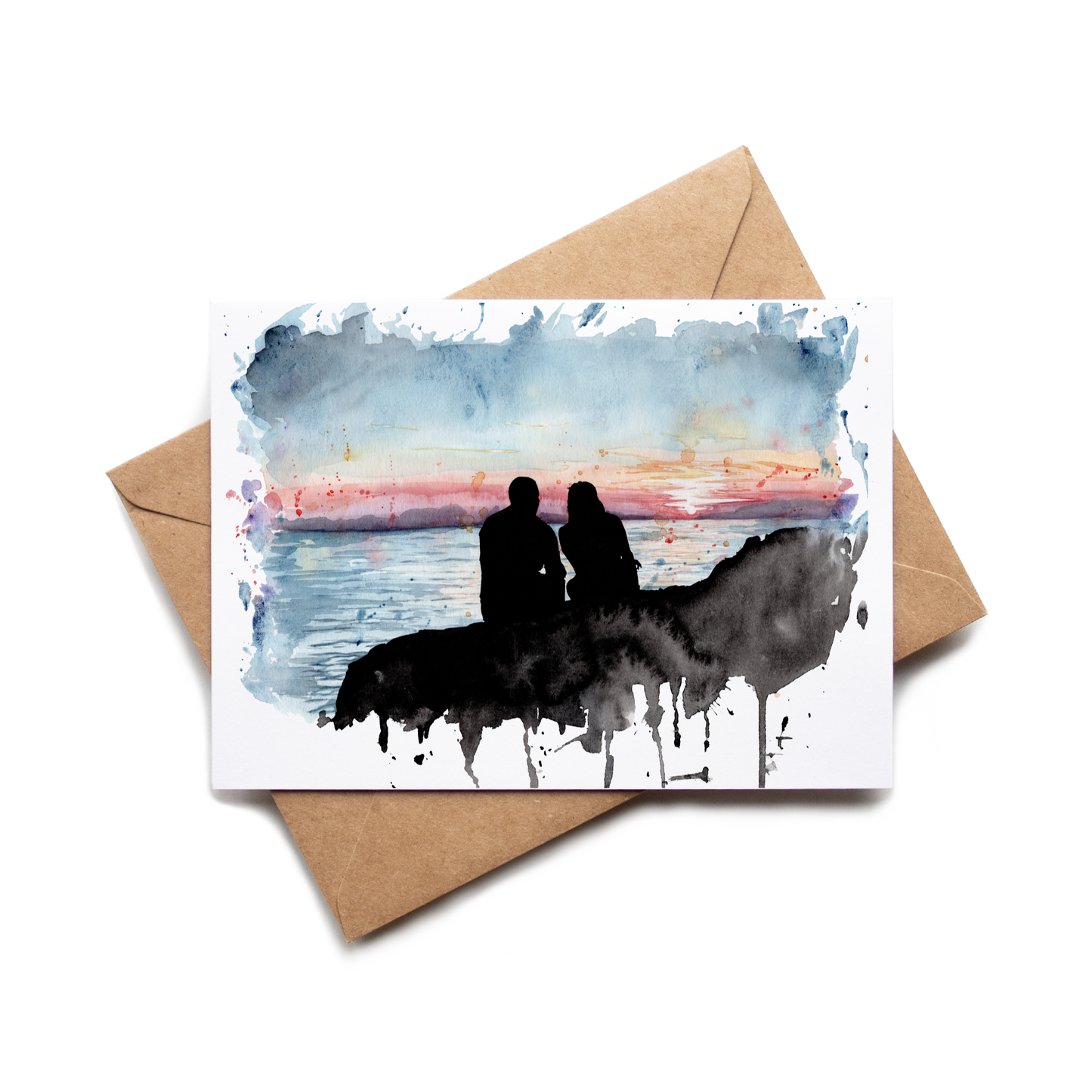 Greeting card with watercolor design of two people on a horse at sunset, placed on a brown envelope.