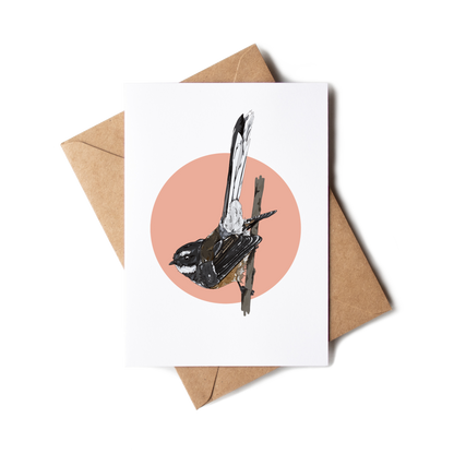 Greeting card with a bird illustration on a pink circle, placed on a white surface with a brown envelope.