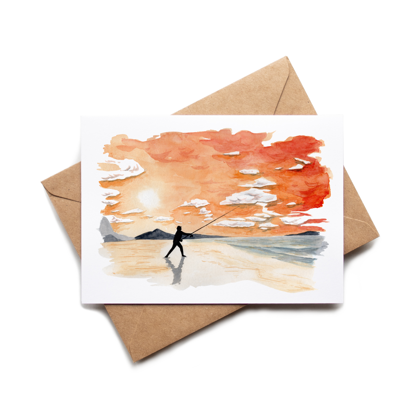 Greeting card with a painting of a person fishing on a beach, placed on a matching brown envelope.