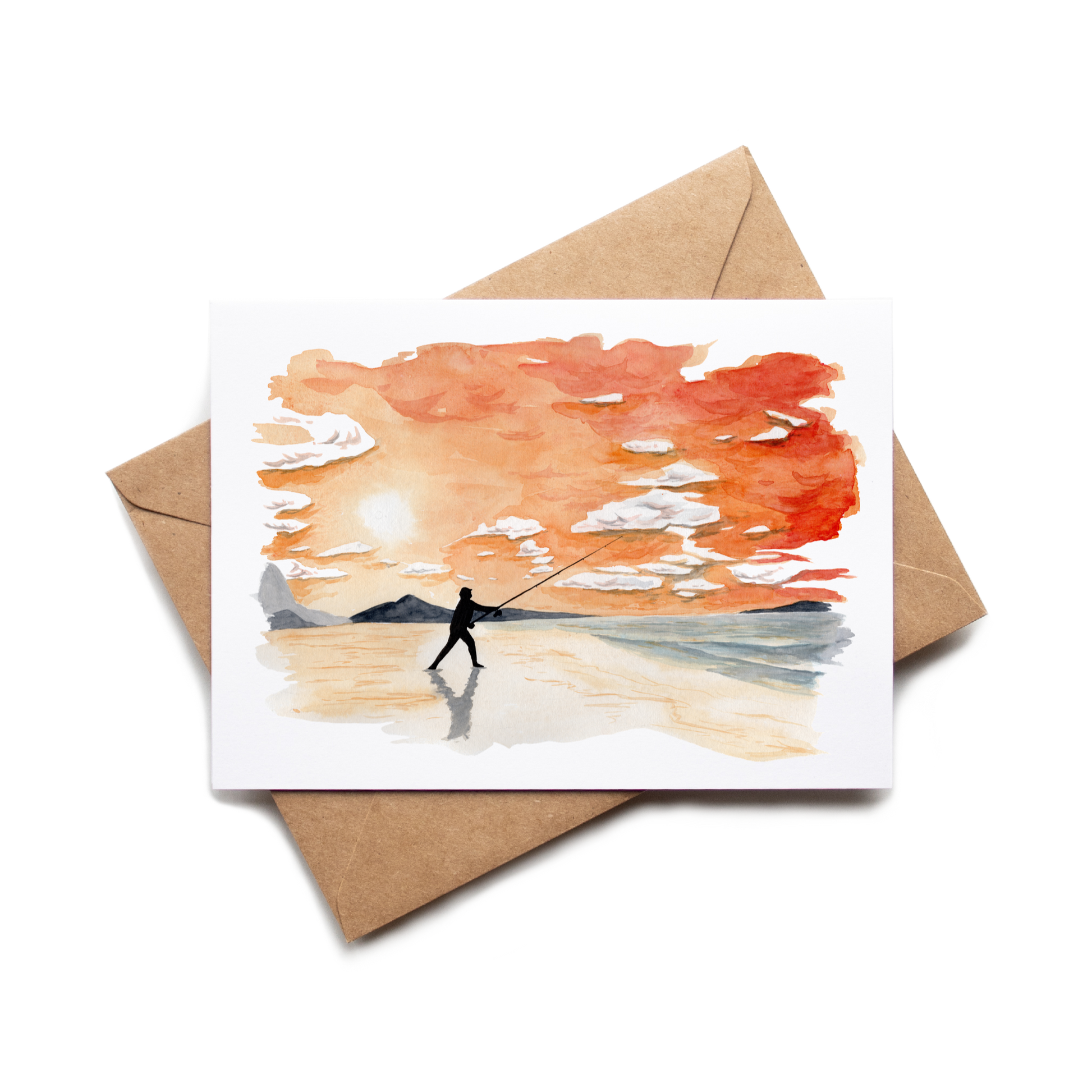 Greeting card with a painting of a person fishing on a beach, placed on a matching brown envelope.