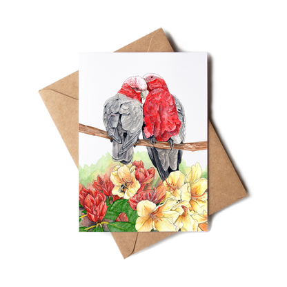 Greeting card with two parrots on a branch and flowers, accompanied by a brown envelope.