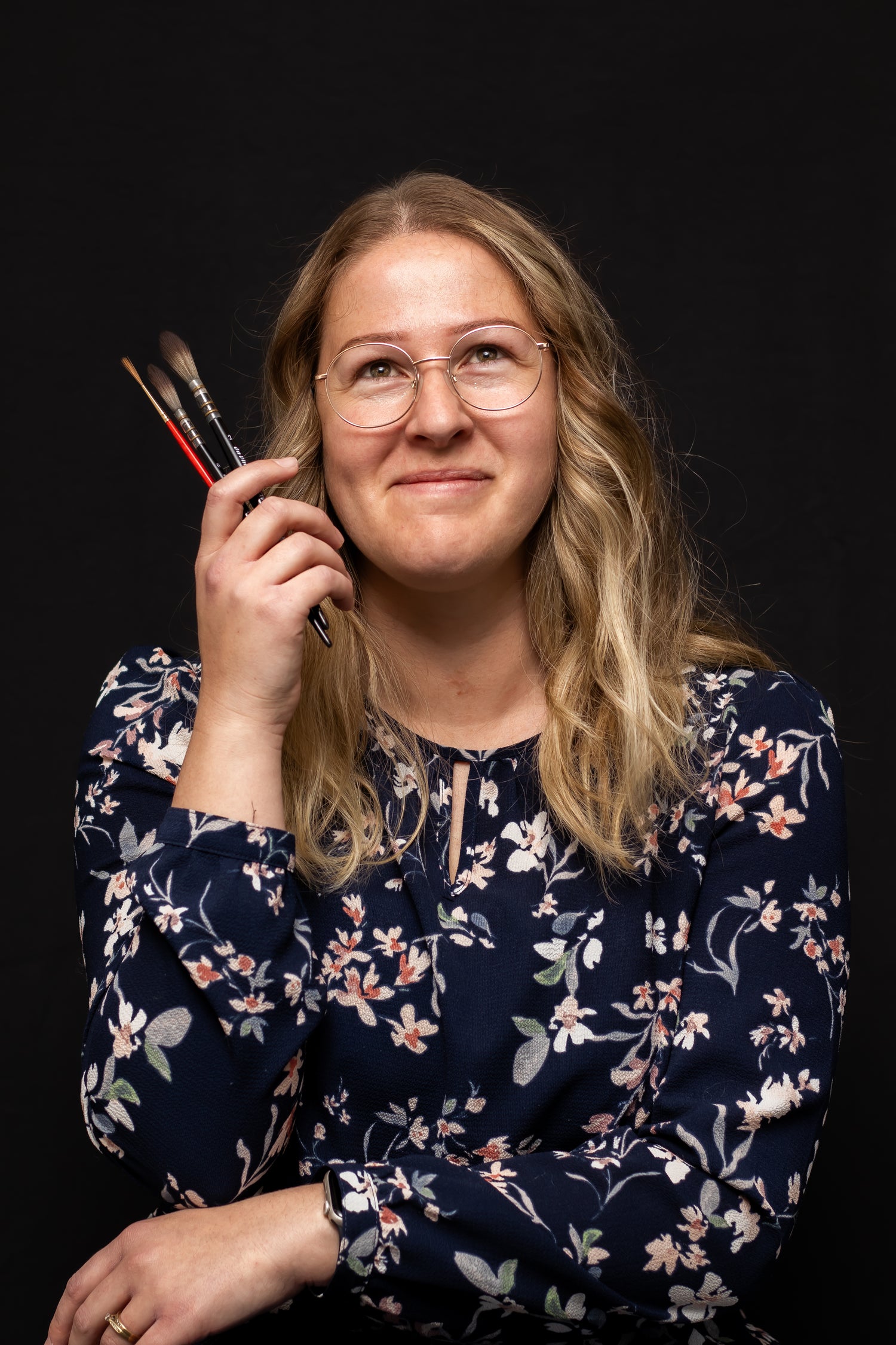 Woman holding paintbrushes against a black background